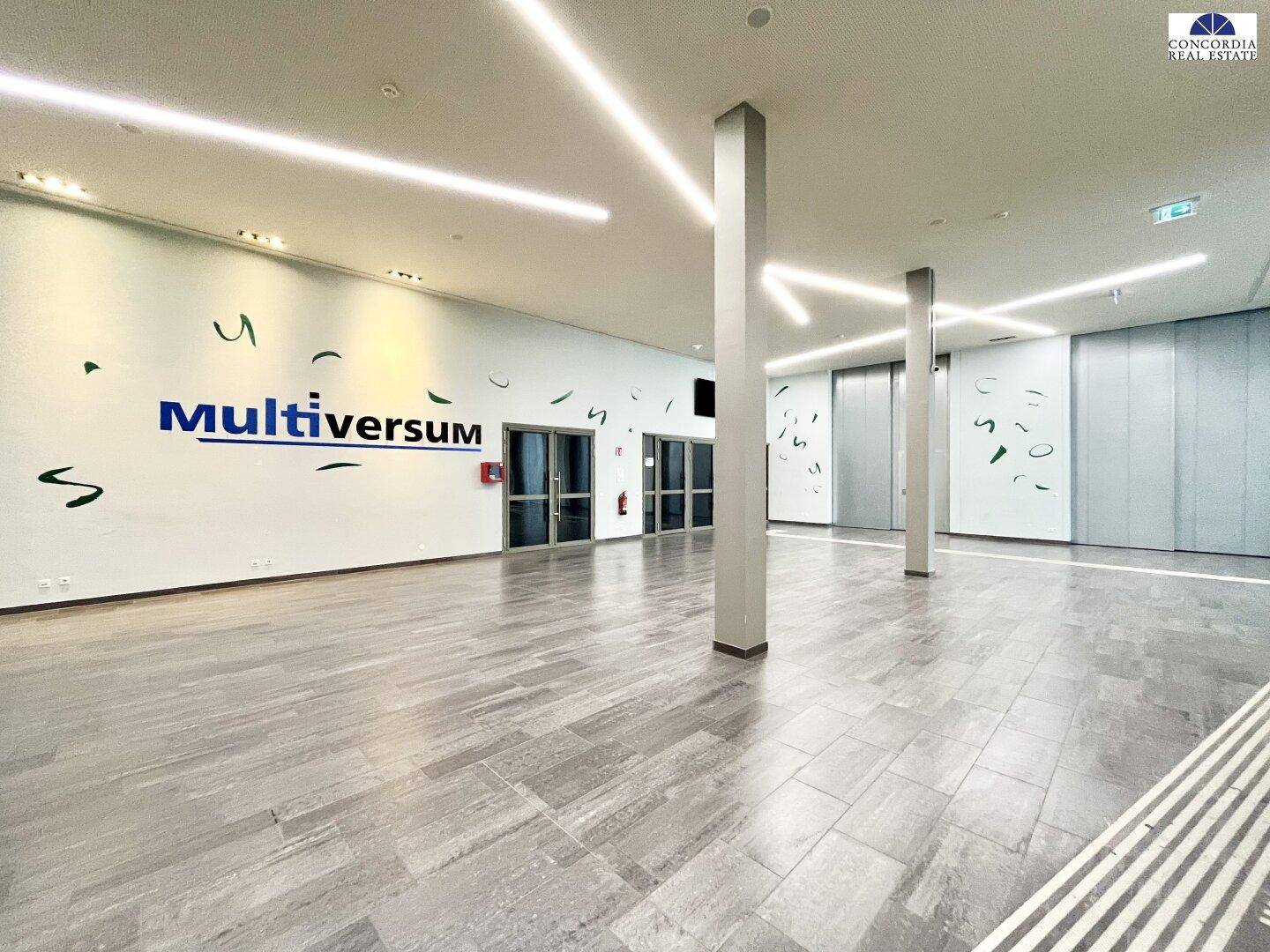 Großer, leerer Saal mit modernen Fliesenböden und hohen Decken, ideal für Veranstaltungen.