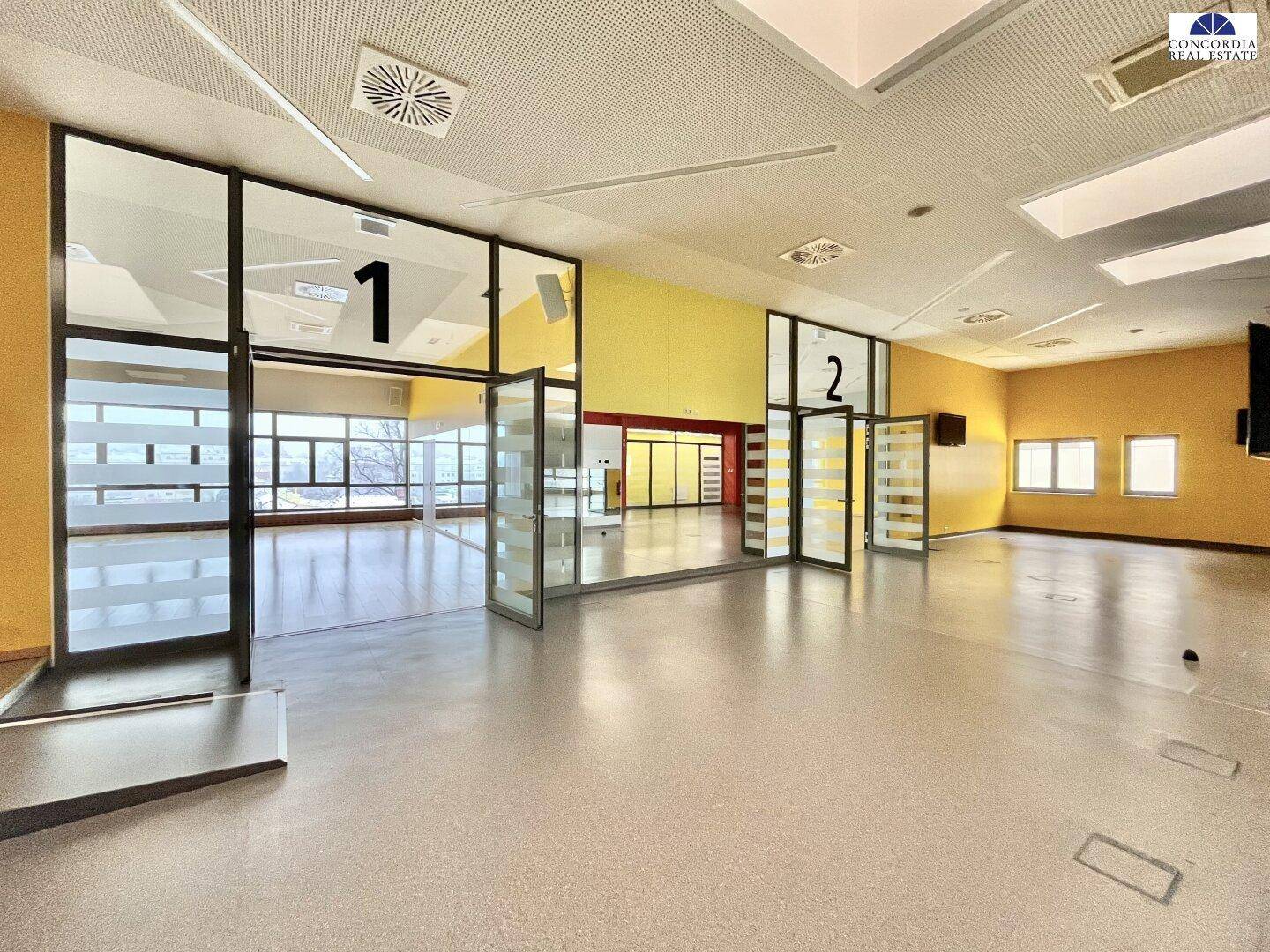 Geräumiger Saal mit großen Glasfronten und Blick nach draußen, ideal für Veranstaltungen.