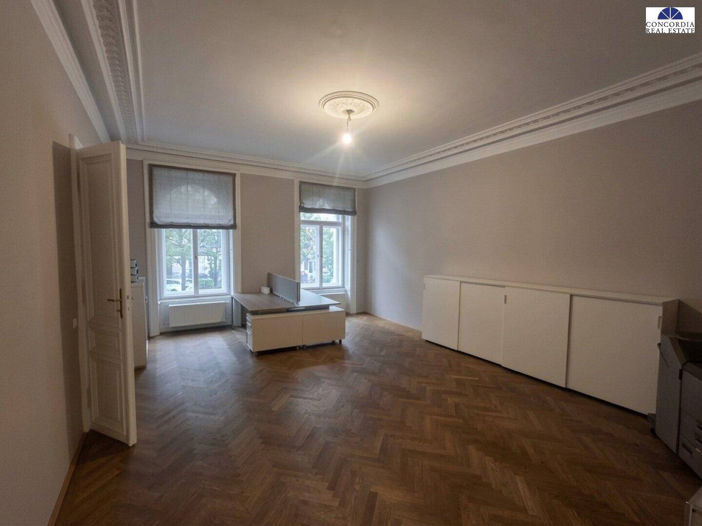 Helles Büro mit Fischgrätparkett, großen Fenstern und integrierten Schränken entlang der Wand.