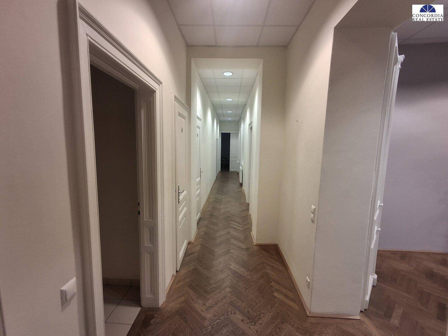 Langer, heller Flur mit Fischgrätparkett und vielen Türen, der verschiedene Büroräume verbindet.
