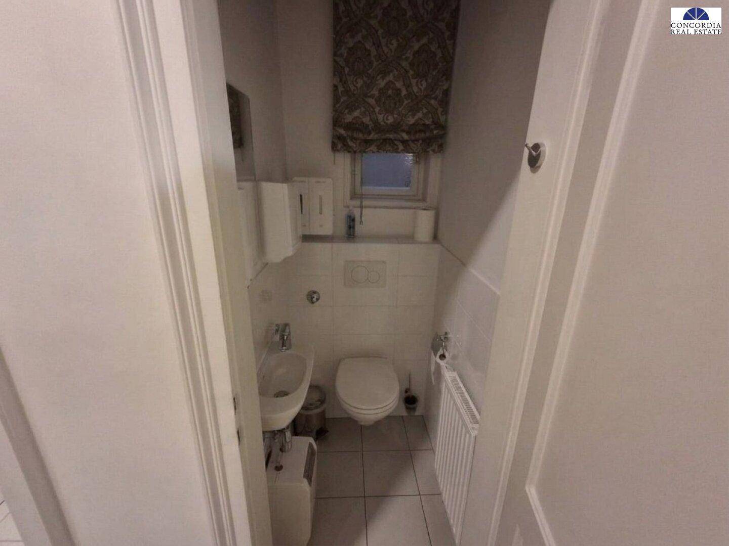 Kleines Gäste-WC mit Wand-WC, Waschbecken und Fenster, ausgestattet mit Fliesenboden.
