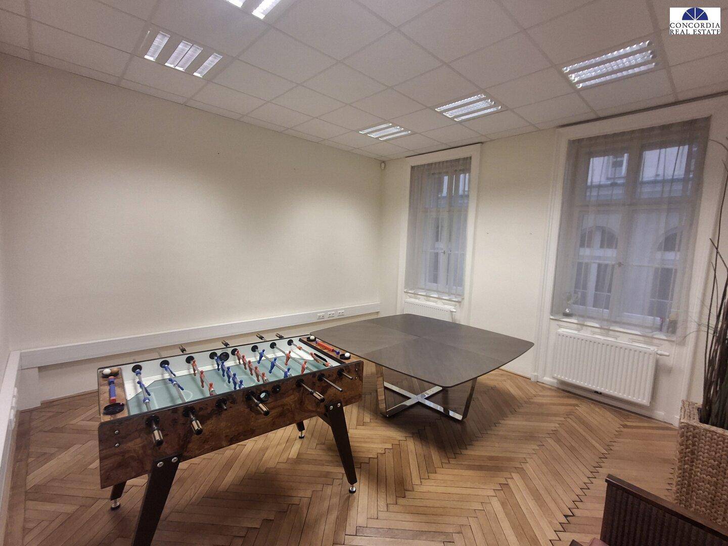 Freizeitraum mit Tischfußball, großem Tisch und Fischgrätparkett, ideal für Pausen.