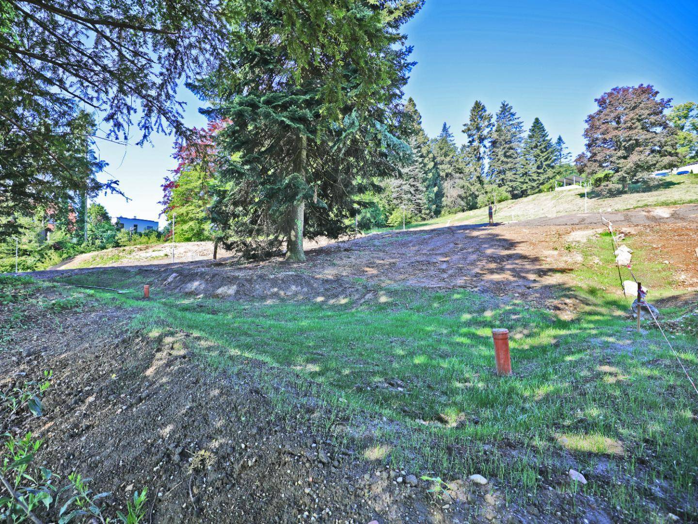 Vorbereitetes Baugrundstück mit jungem Rasen und Markierungen für Versorgungsleitungen unter blauem Himmel.