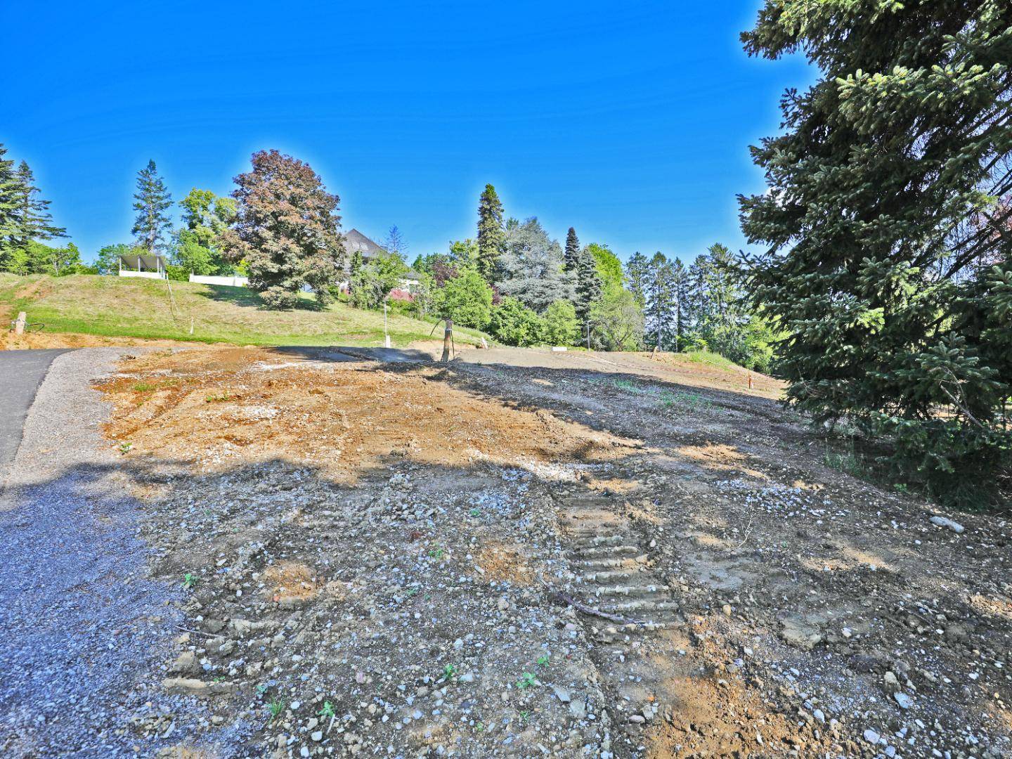 Weitläufiges Baugrundstück mit vorbereitetem Untergrund, umgeben von Bäumen unter blauem Himmel.