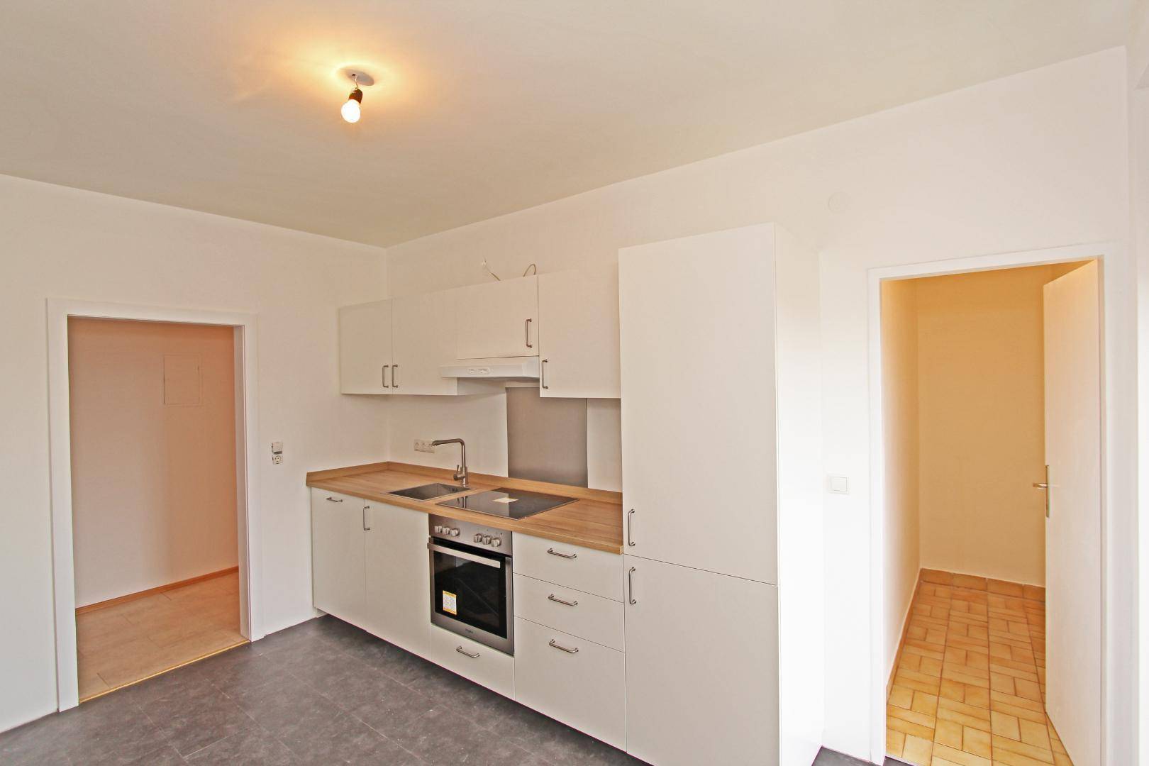 Funktionale Küche mit weißen Schränken und Holztheke, angrenzend an weitere Räume.