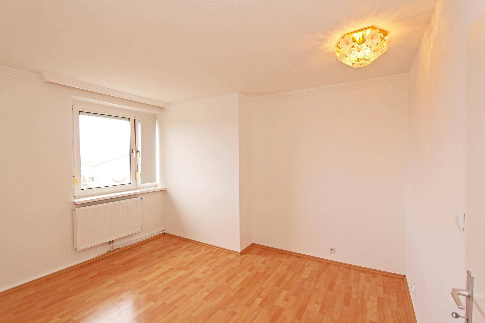 Helles Zimmer mit Parkettboden und Fenster, bereit zur individuellen Gestaltung.