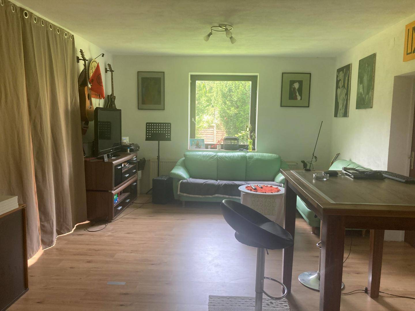 Geräumiges Wohnzimmer mit Laminatboden, grünen Sofas und Blick auf die umliegende Natur.