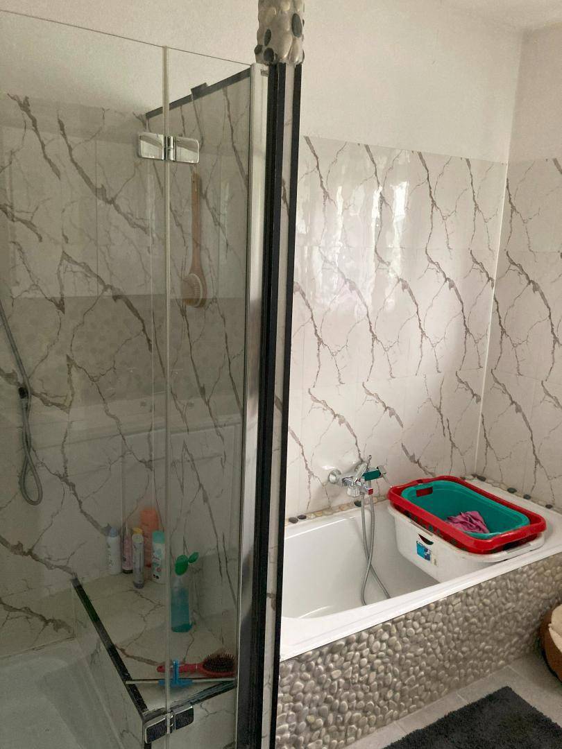 Badezimmer mit Badewanne, Duschkabine und gemusterten Fliesen an den Wänden.