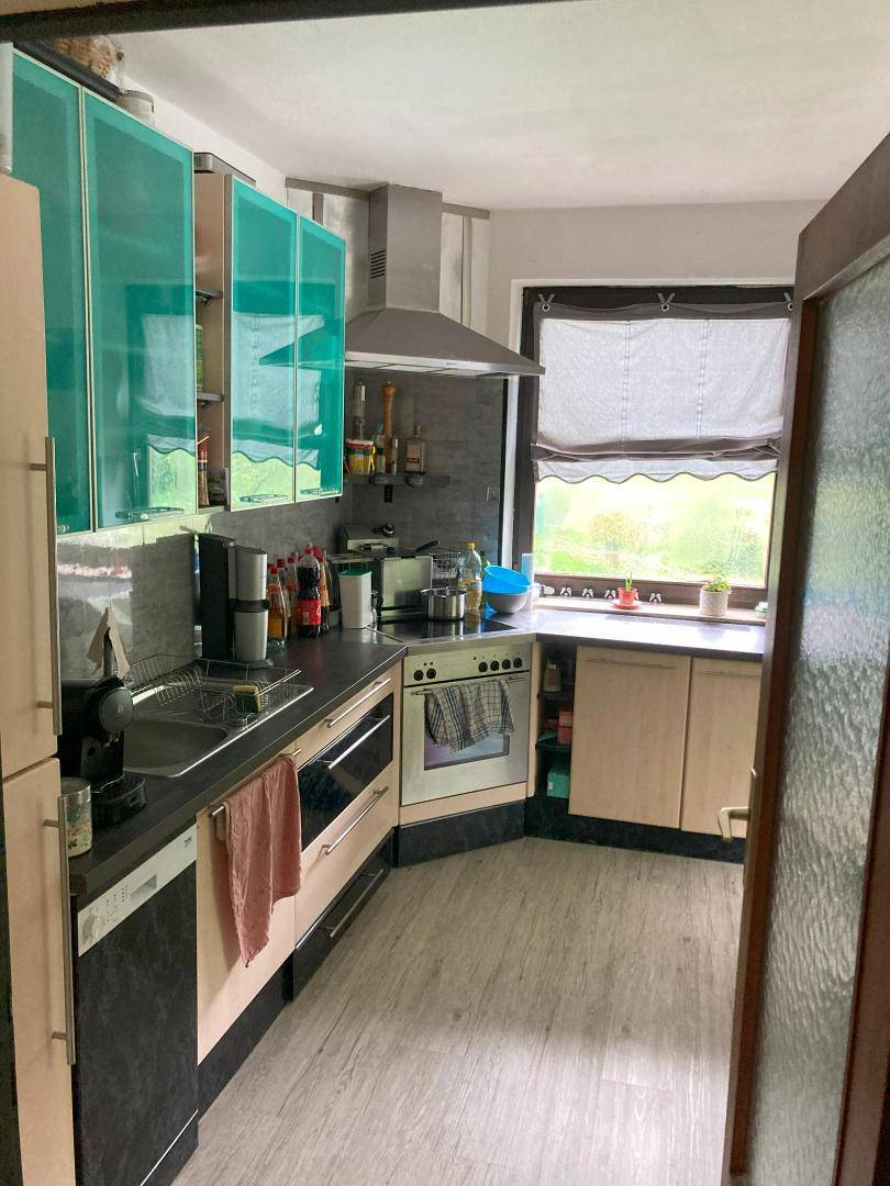 Küche mit türkisfarbenen Oberschränken, dunkler Arbeitsplatte und Fensterblick ins Grüne.