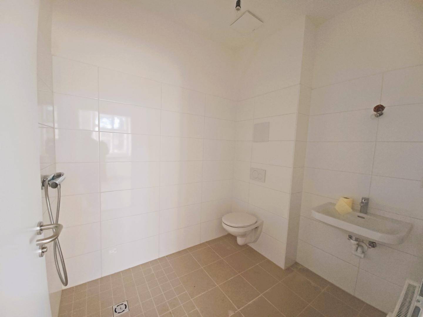 Modernes Badezimmer mit ebenerdiger Dusche, wandhängendem WC und weißen Fliesen an Wänden und Boden.