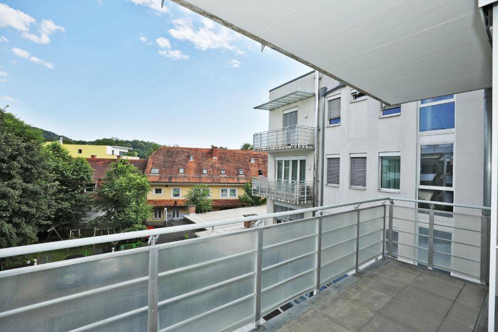 Geräumiger Balkon mit Metallgeländer und Blick auf benachbarte Gebäude und grüne Umgebung.