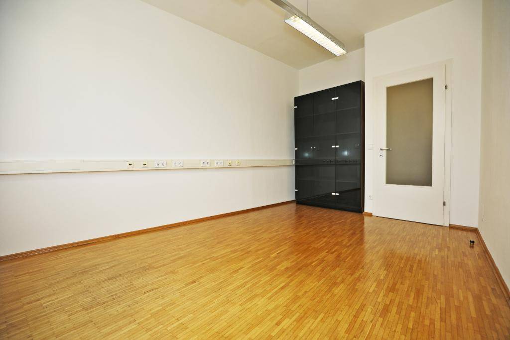 Büroraum mit Parkettboden, weißer Wand und einem schwarzen Schrank, der Stauraum bietet.