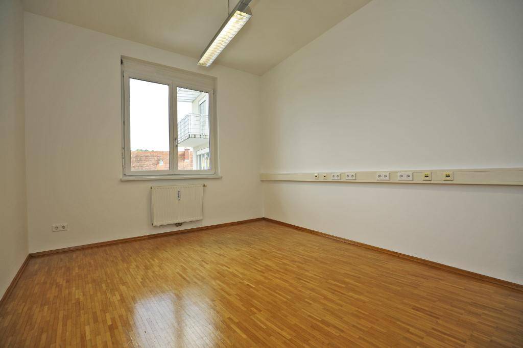 Büroraum mit Parkettboden und Fenster, das einen Blick auf die umliegenden Gebäude ermöglicht.