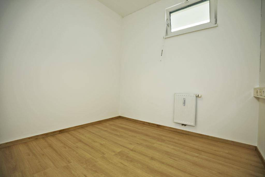 Leerer Raum mit Laminatboden und kleinem Fenster, das für Belüftung und Licht sorgt.