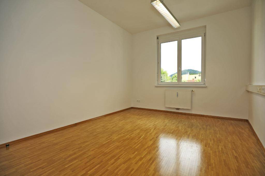 Kleiner Büroraum mit hellem Parkettboden und einem Fenster, das Tageslicht hereinlässt.