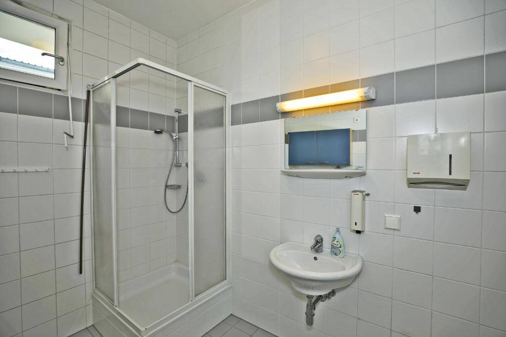 Gefliestes Badezimmer mit Duschkabine, Waschbecken und Fenster, in hellen Farben gestaltet.