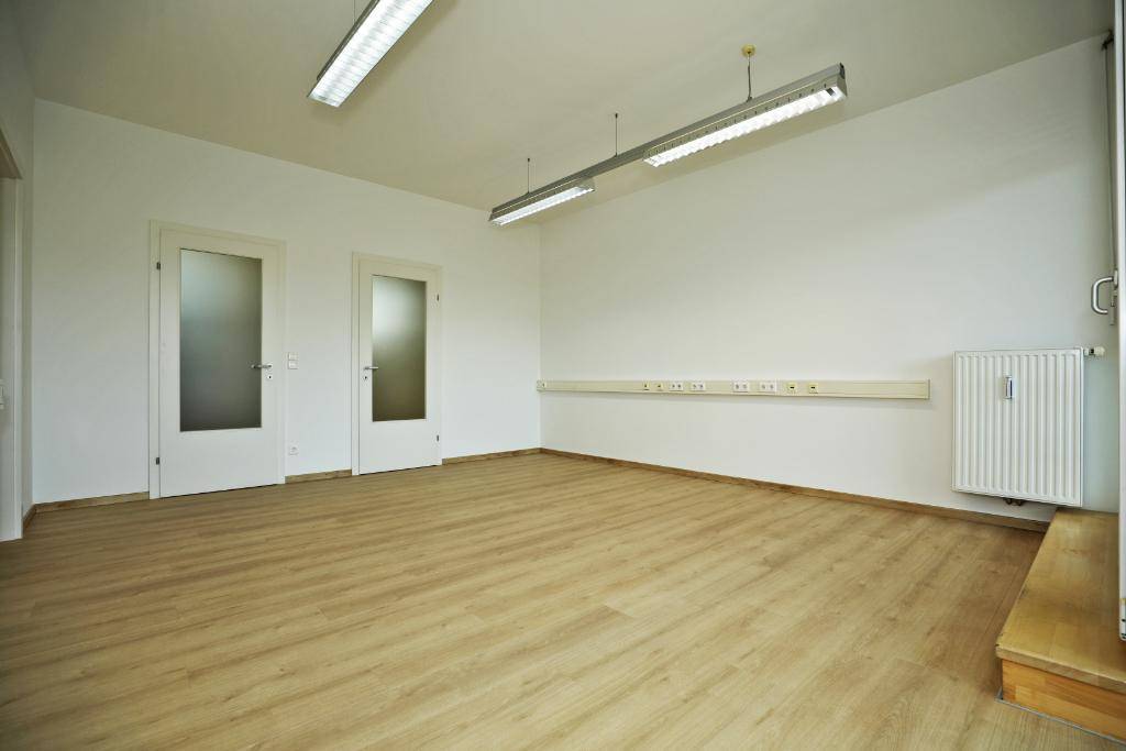 Heller Büroraum mit Laminatboden, weißen Wänden und Heizkörper, bereit zur individuellen Gestaltung.