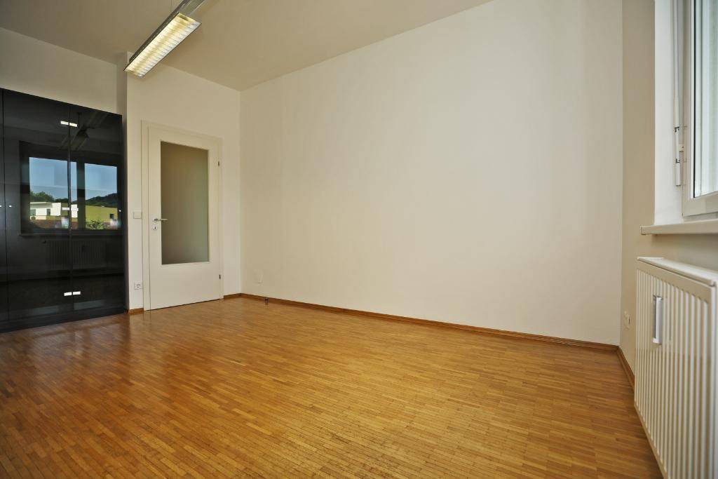 Heller Büroraum mit Parkettboden, Fenster und einem schwarzen Schrank, der sich gut einfügt.