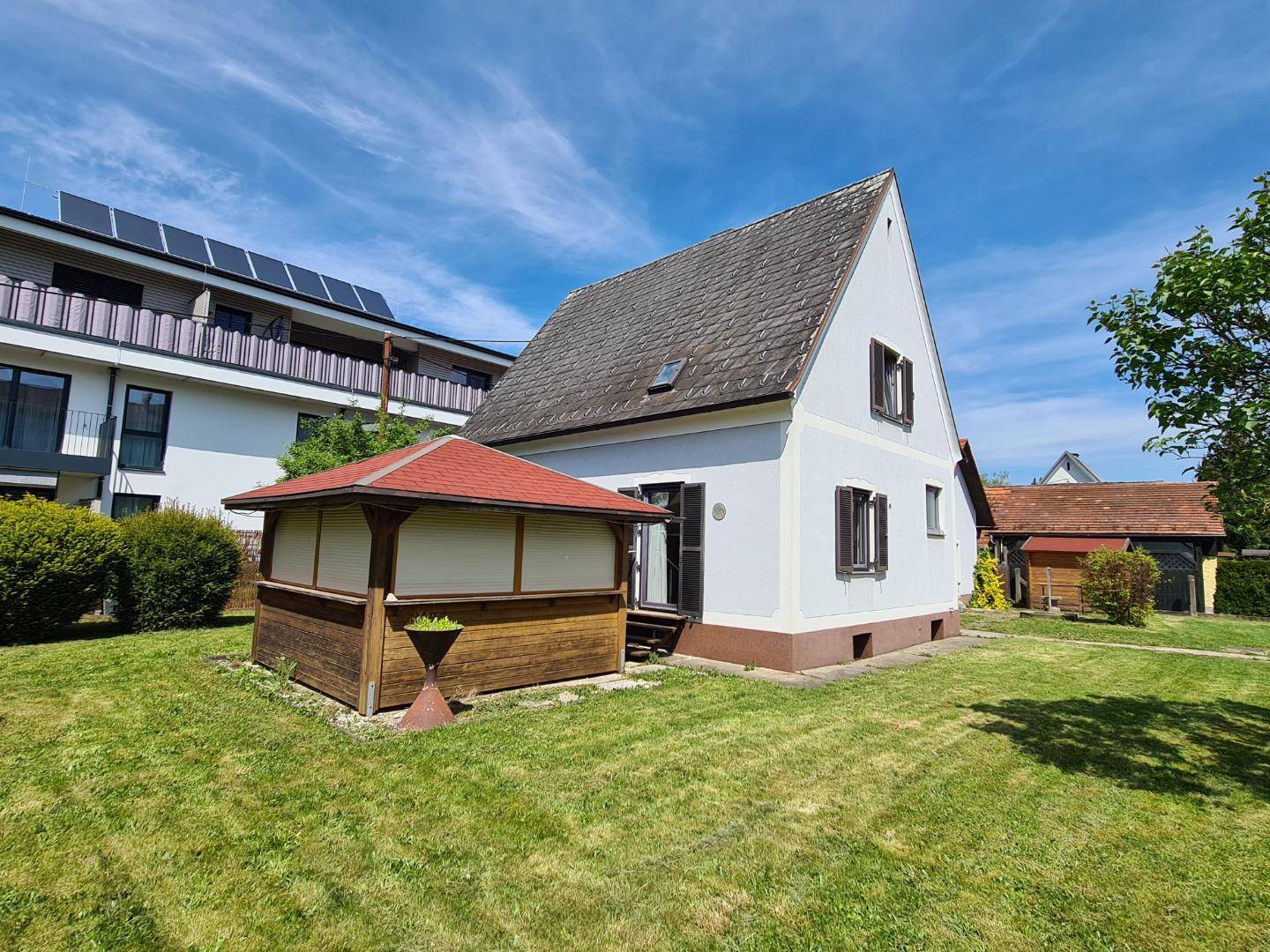 Rückseite des Hauses mit Garten, Gartenlaube und angrenzendem Gebäude mit Solaranlage.