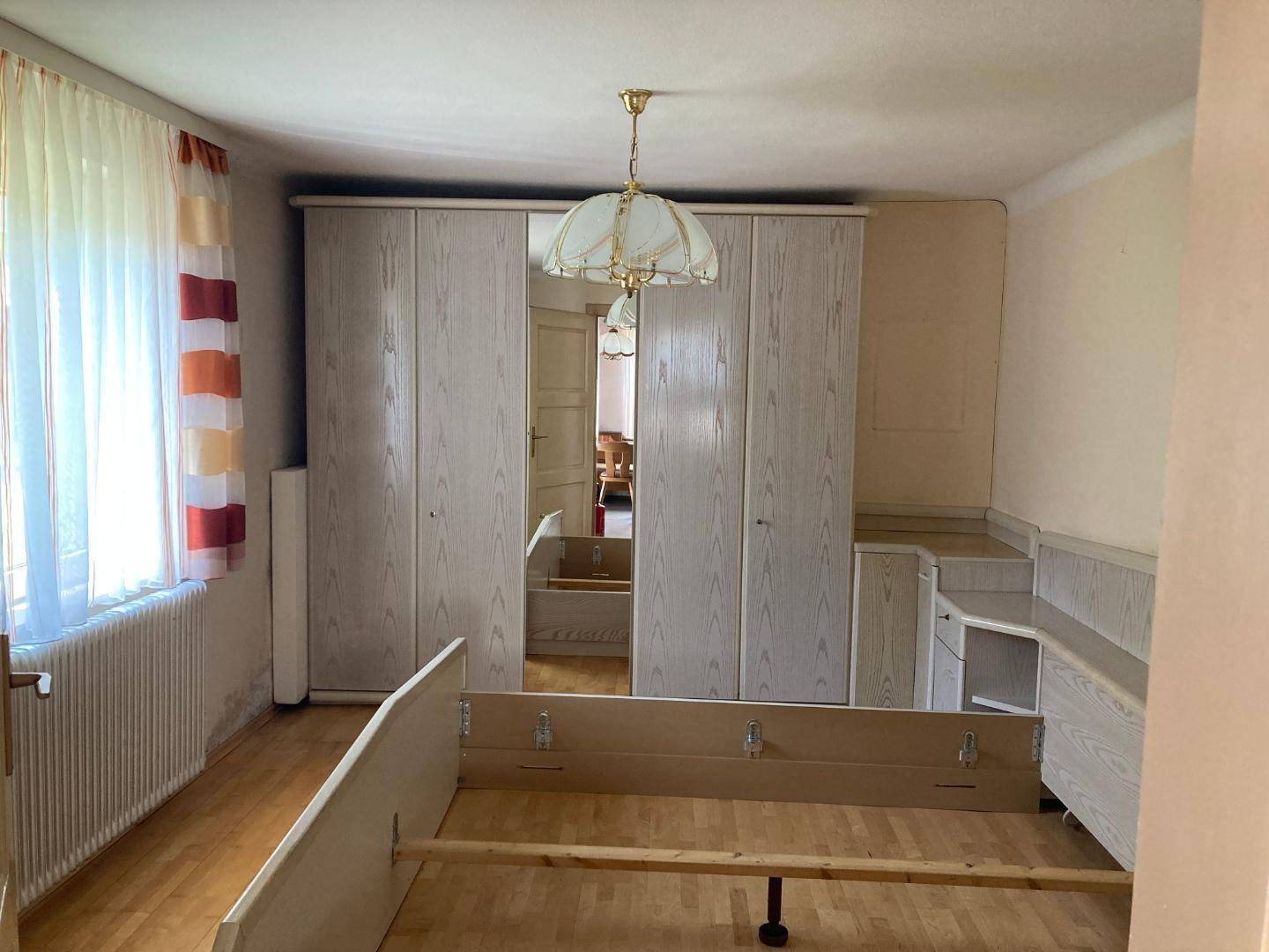 Schlafzimmer mit Bettgestell, großem Kleiderschrank und hellem Parkettboden.