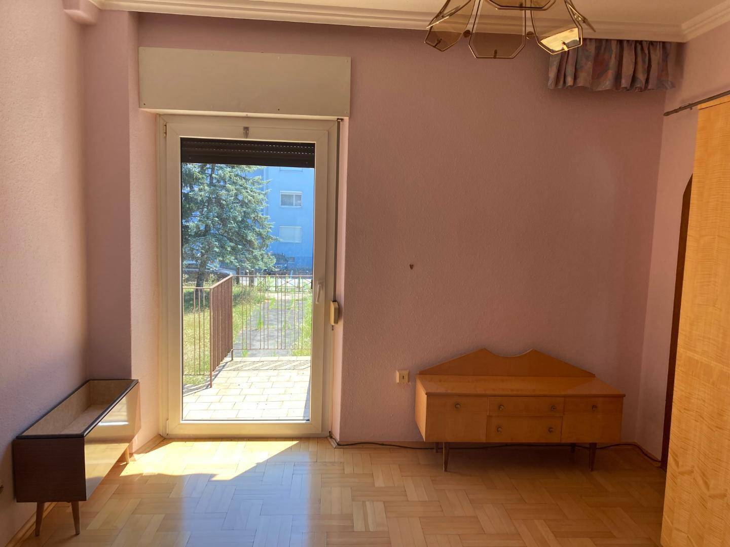 Leeres Zimmer mit Zugang zu einem kleinen Balkon und Fischgrätparkettboden.