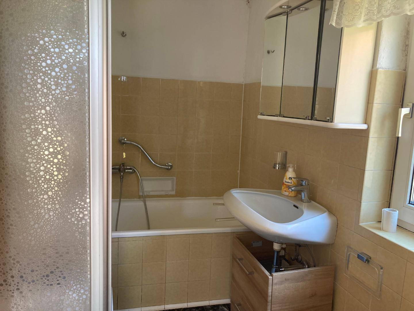 Badezimmer im Stil der 80er Jahre mit Badewanne, Waschbecken und Spiegelschrank.