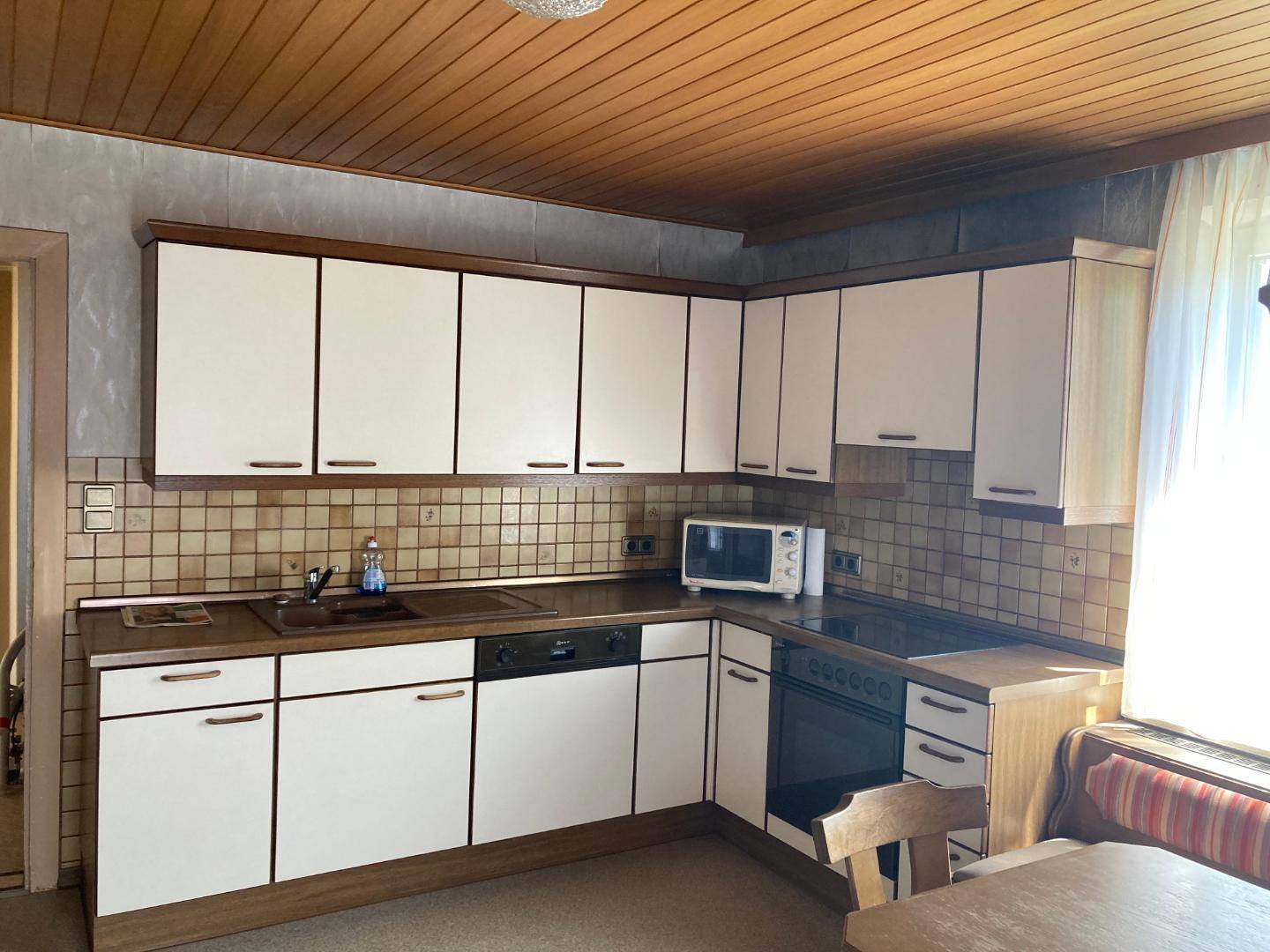 Küche im Landhausstil mit weißen Schränken, gefliestem Spritzschutz und Holzbalkendecke.