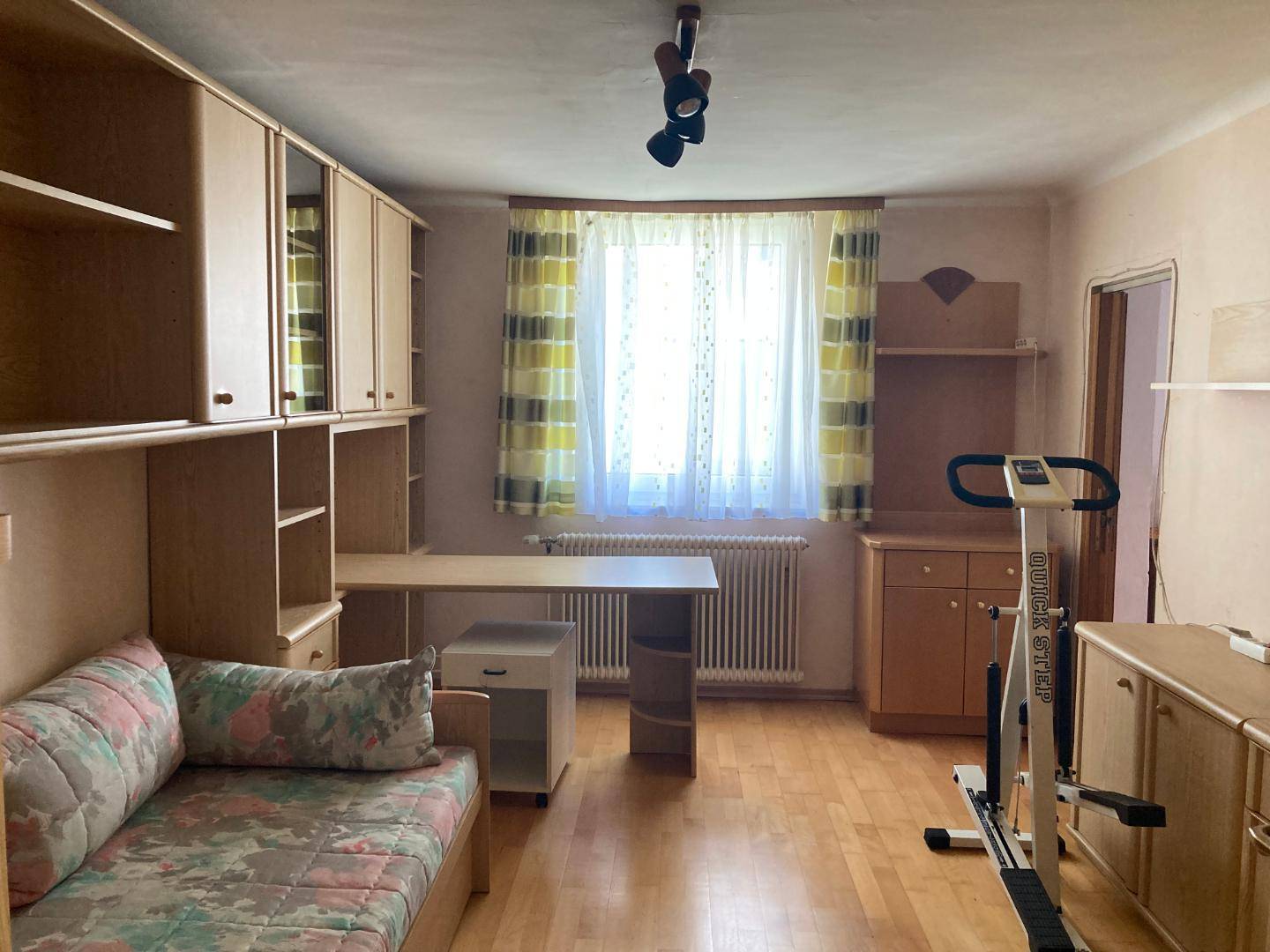 Schlafzimmer mit Einzelbett, Schreibtisch und Fitnessgerät, ausgestattet mit Holzparkett.