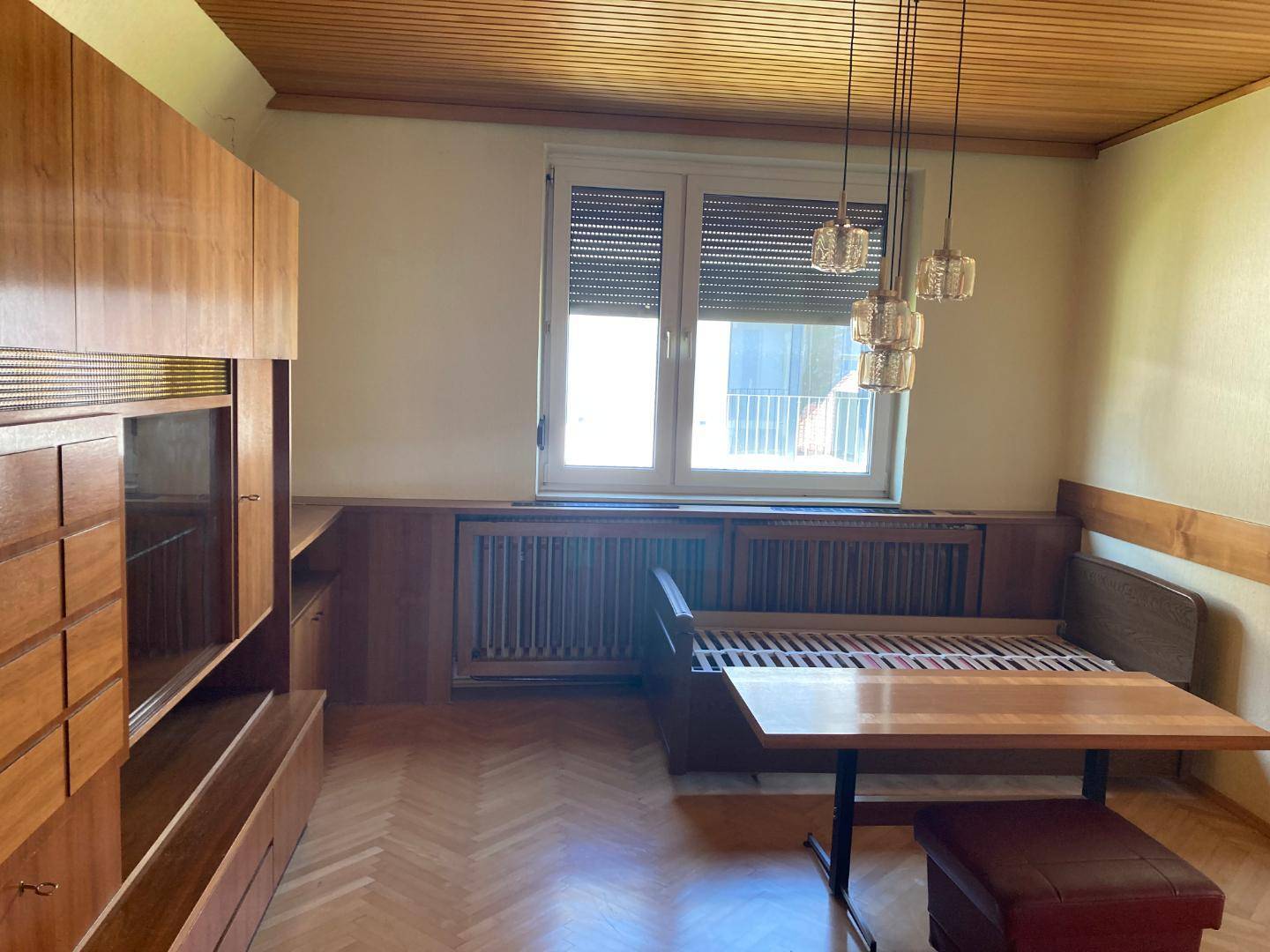 Wohnraum mit Holzmöbeln, Schlafsofa und großem Fenster mit Jalousien.