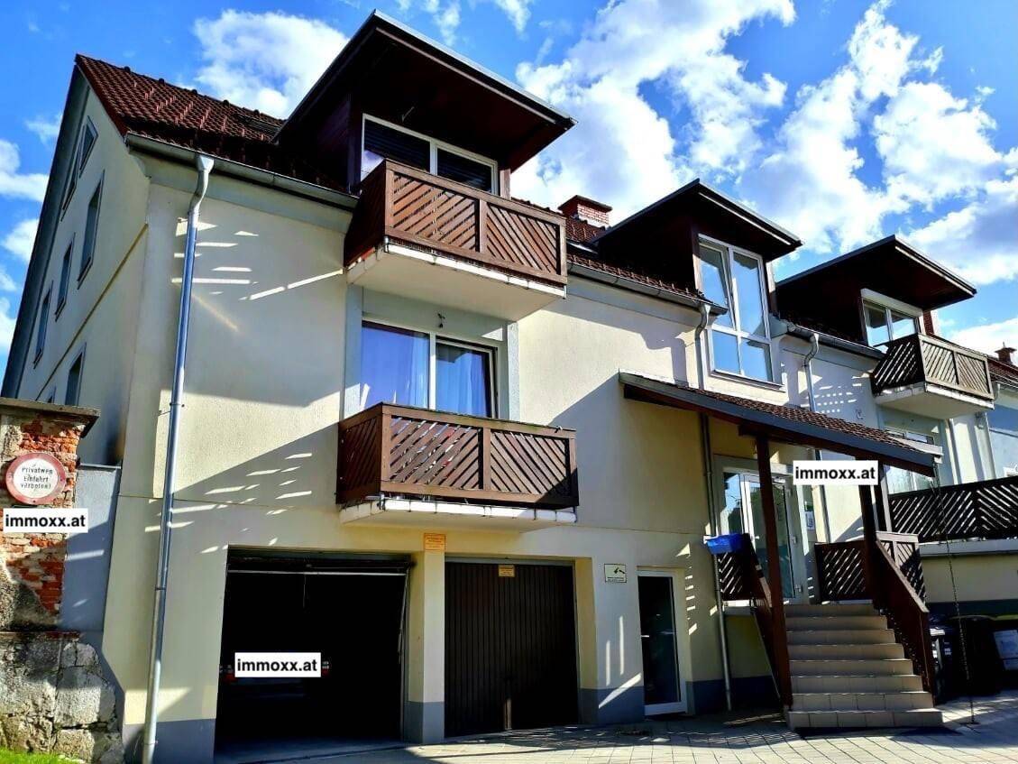 Mehrfamilienhaus mit mehreren Balkonen, Garagen und traditioneller Architektur unter blauem Himmel.