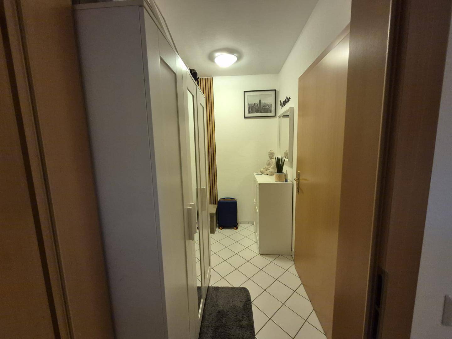 Schmaler Flur mit Spiegelschrank, Fliesenboden und Zugang zu weiteren Räumen.