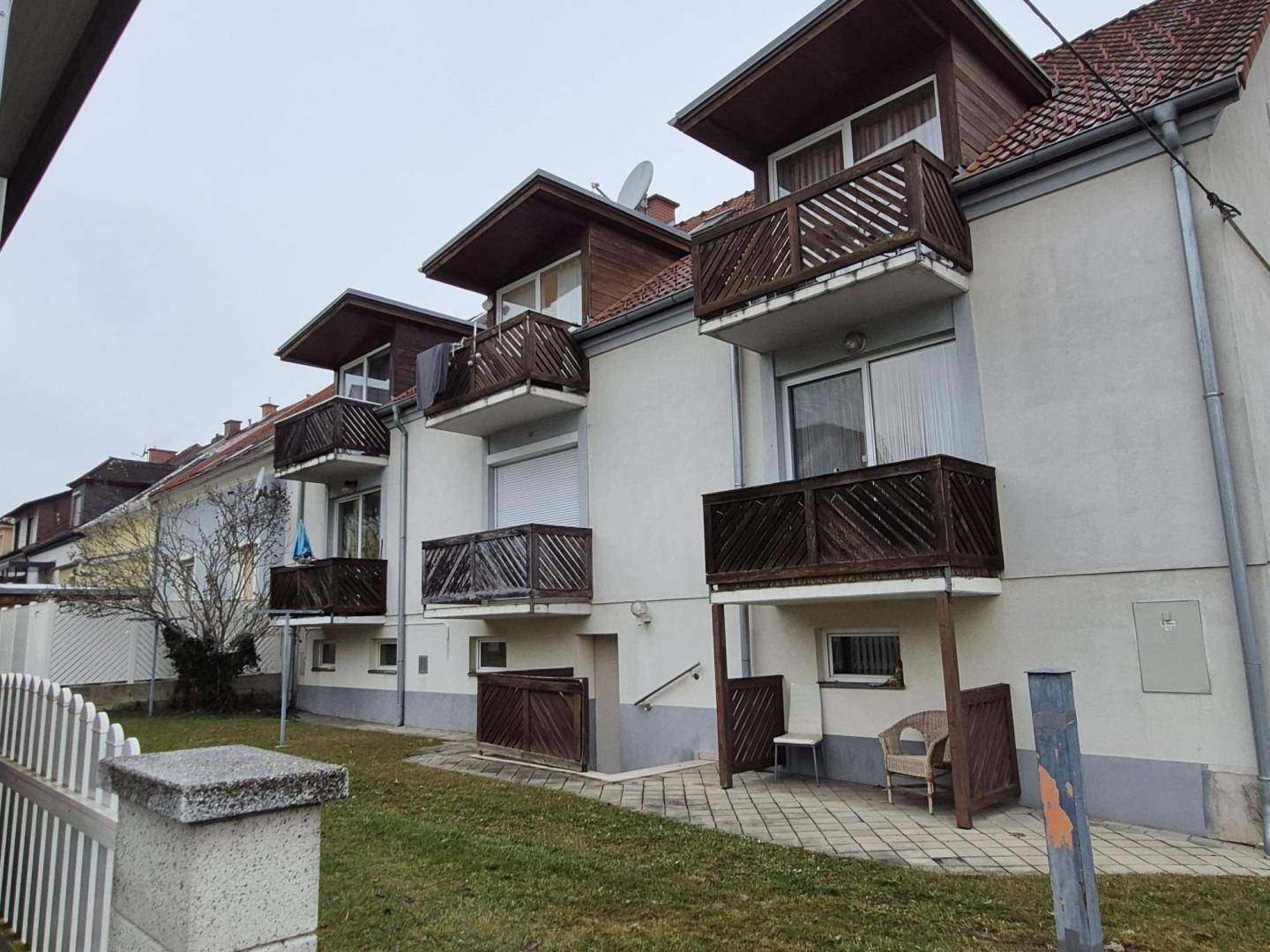 Rückseite eines Mehrfamilienhauses mit Balkonen, kleinem Gartenbereich und gepflasterter Terrasse.