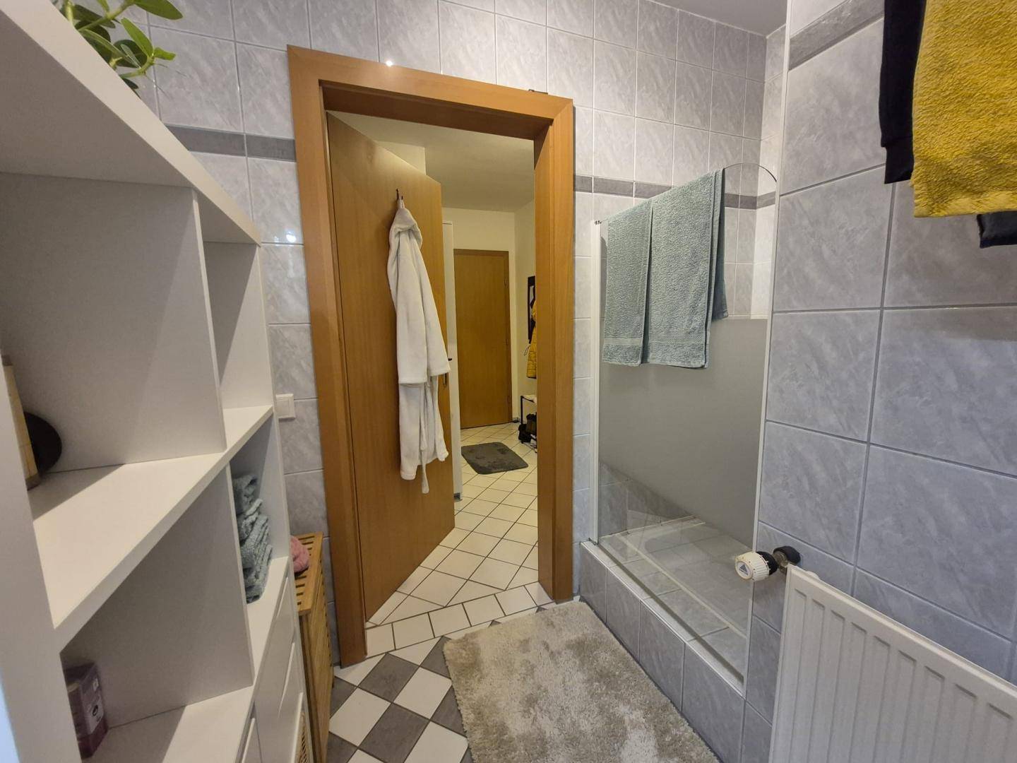 Badezimmer mit Duschbereich, Fliesenboden und praktischen Handtuchhaltern.