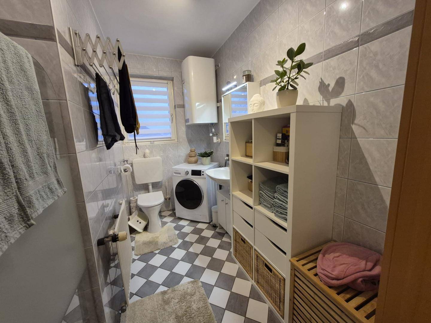 Modernes Badezimmer mit Waschmaschine, Duschbereich und grau-weißem Fliesenmuster.