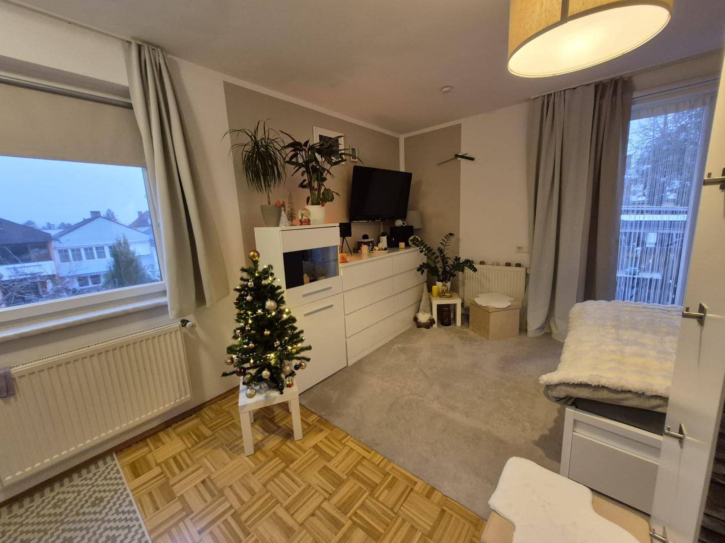 Helles Schlafzimmer mit zwei Fenstern, Teppichboden und festlicher Weihnachtsdekoration.