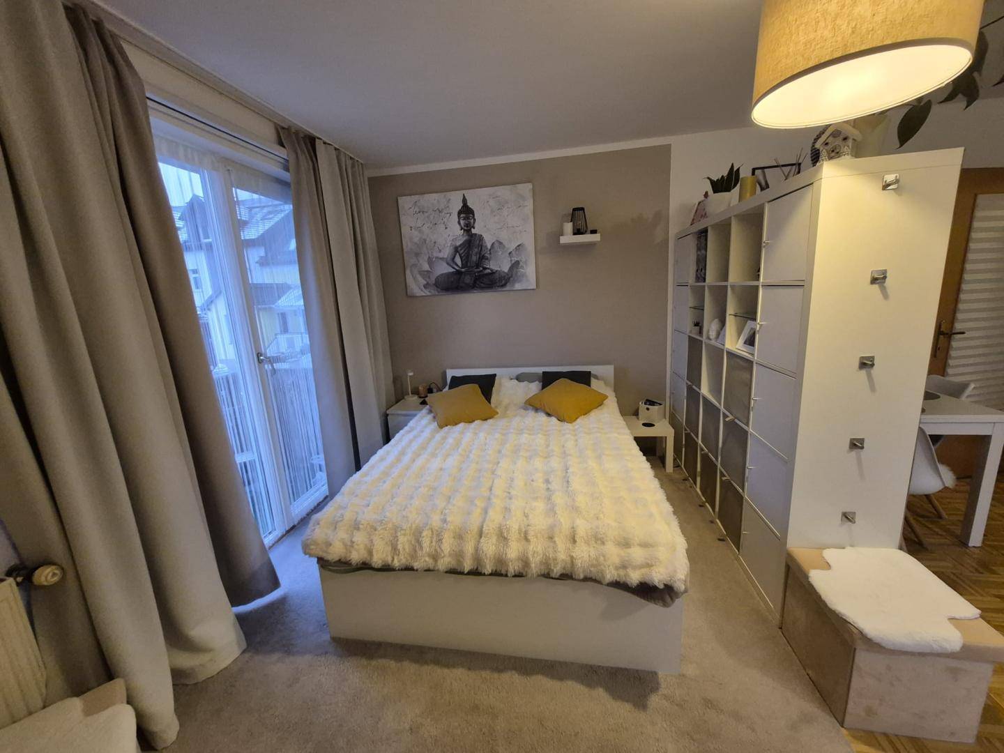 Schlafzimmer mit großem Bett, offenem Regal und Zugang zum Balkon.