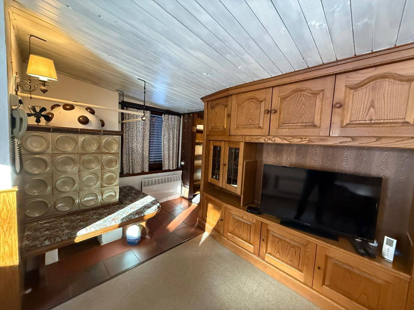 Gemütliches Wohnzimmer mit Holzwänden, einem Kachelofen und einem großen Holzschrank mit integriertem Fernseher.