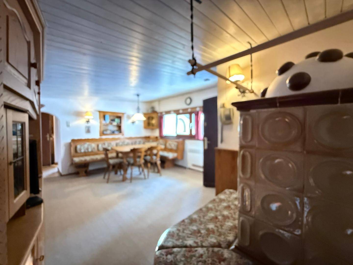 Geräumiger Wohn-Essbereich mit traditionellen Holzmöbeln, einem Kachelofen und einem Essbereich im Hintergrund.