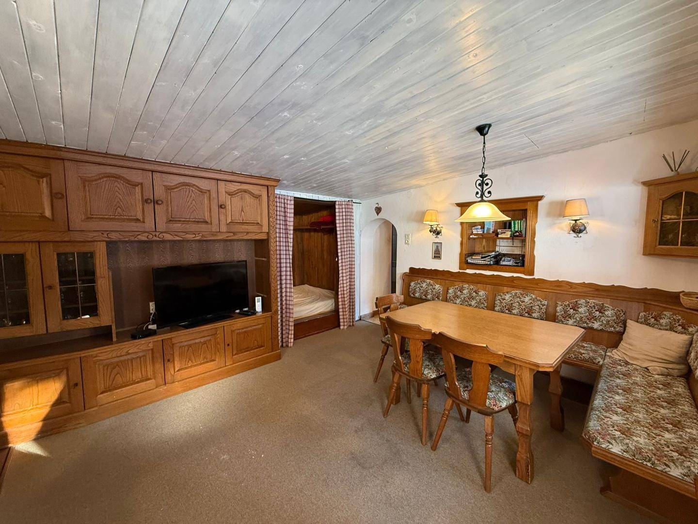 Geräumiger Wohn-Essbereich mit traditionellen Holzmöbeln, einem Kachelofen und einem integrierten Schlafbereich.