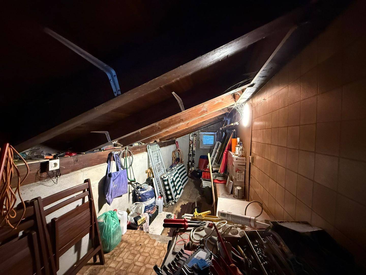 Unaufgeräumter Dachboden mit sichtbaren Holzbalken, Fliesenboden und verschiedenen Gegenständen.