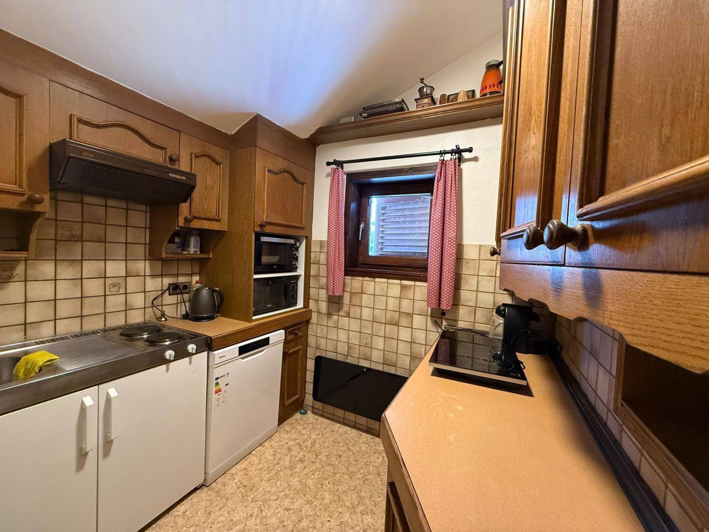 Rustikale Küche mit Holzschränken, beigen Fliesen und integrierten Geräten, darunter ein Backofen und ein Kühlschrank.