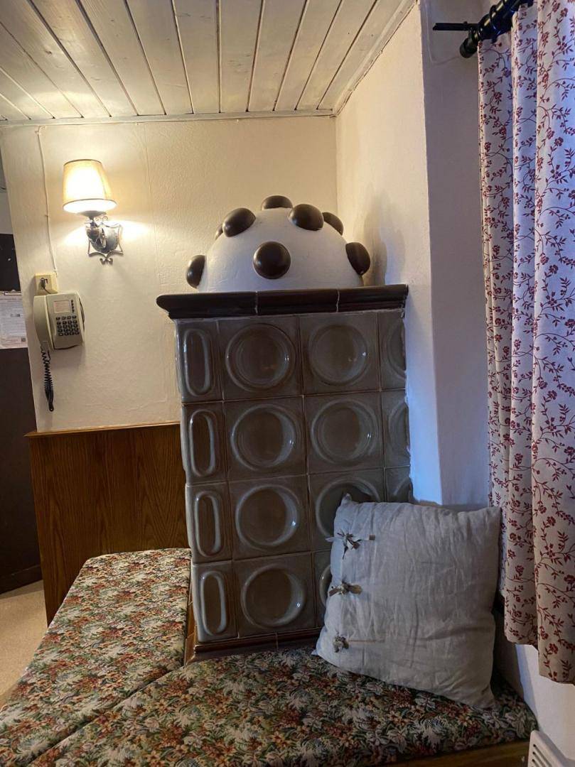 Detailansicht eines traditionellen Kachelofens mit Sitzbank und Vorhängen im Hintergrund.