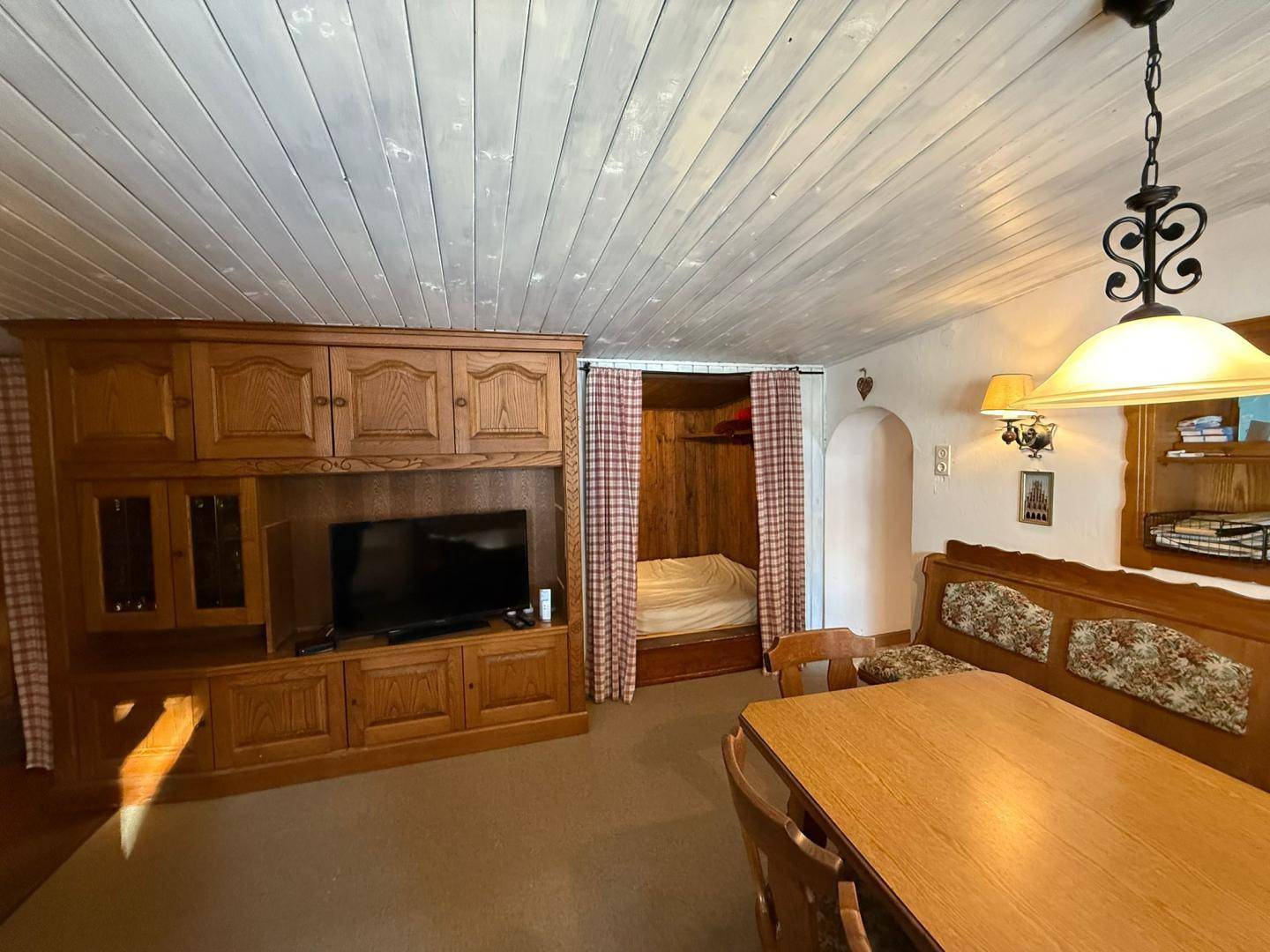 Gemütlicher Wohn-Essbereich mit traditionellen Holzmöbeln, einem Kachelofen und einem integrierten Schlafbereich.