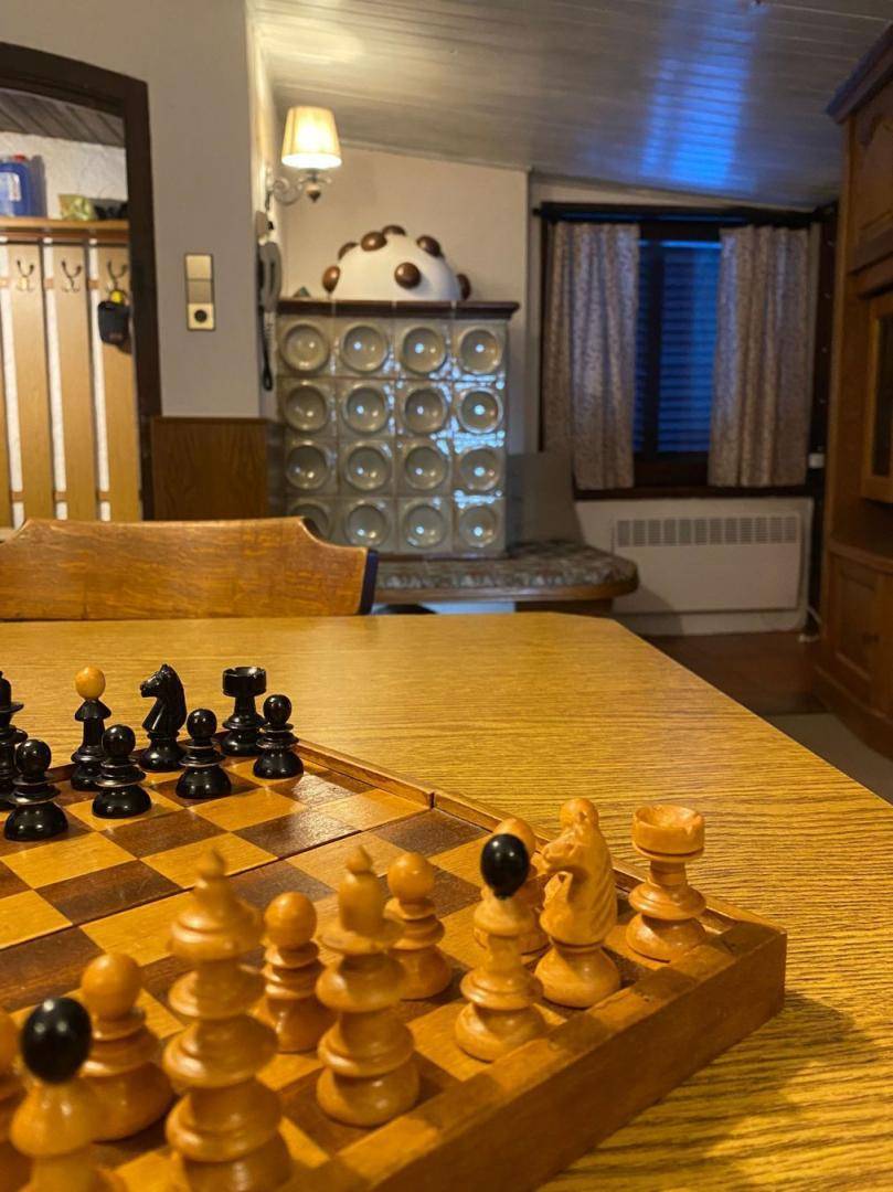 Schachbrett auf einem Holztisch im traditionellen Wohnbereich mit Kachelofen im Hintergrund.