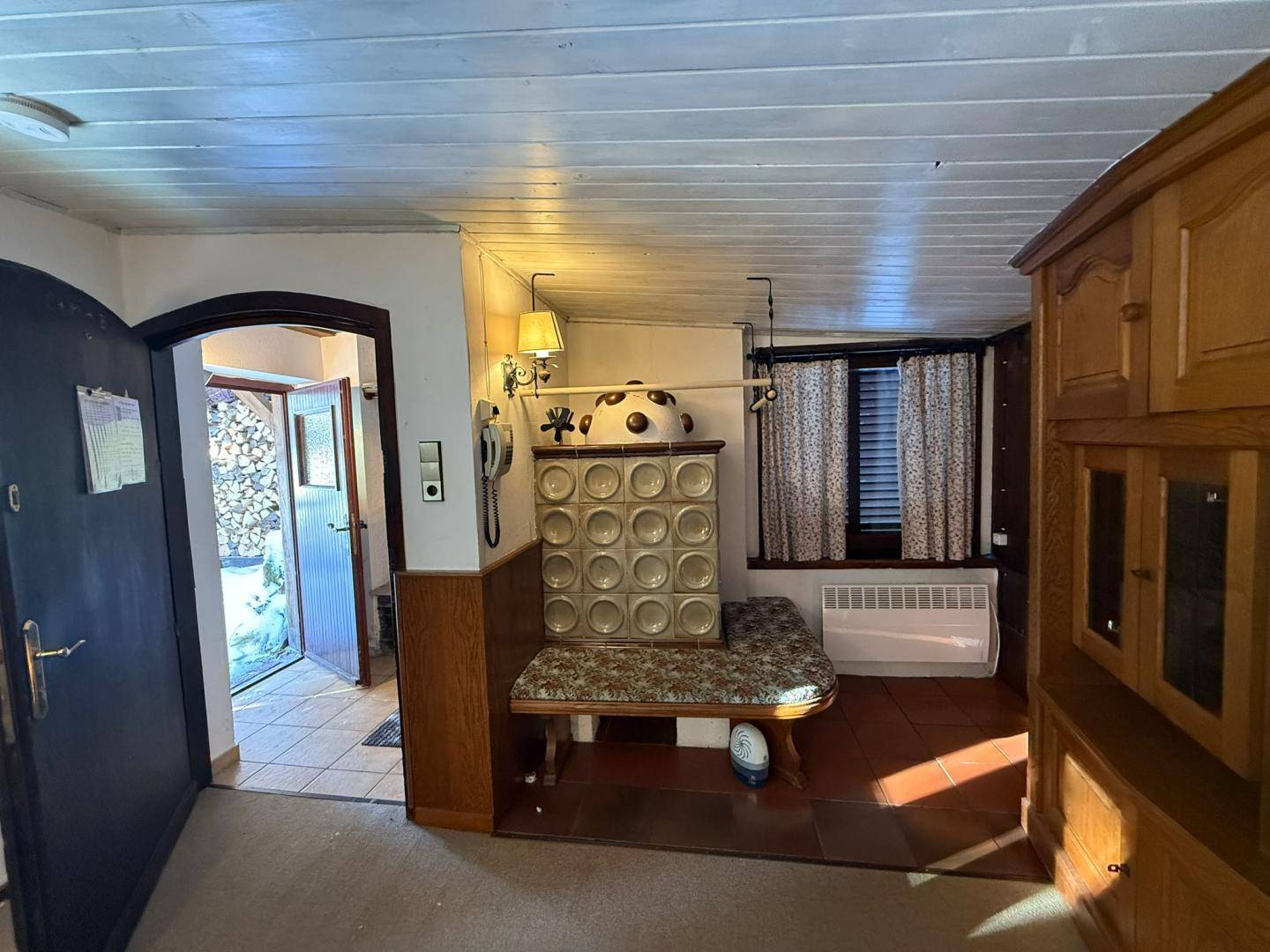 Eingangsbereich mit Kachelofen, Fliesenboden und Zugang zu weiteren Räumen.