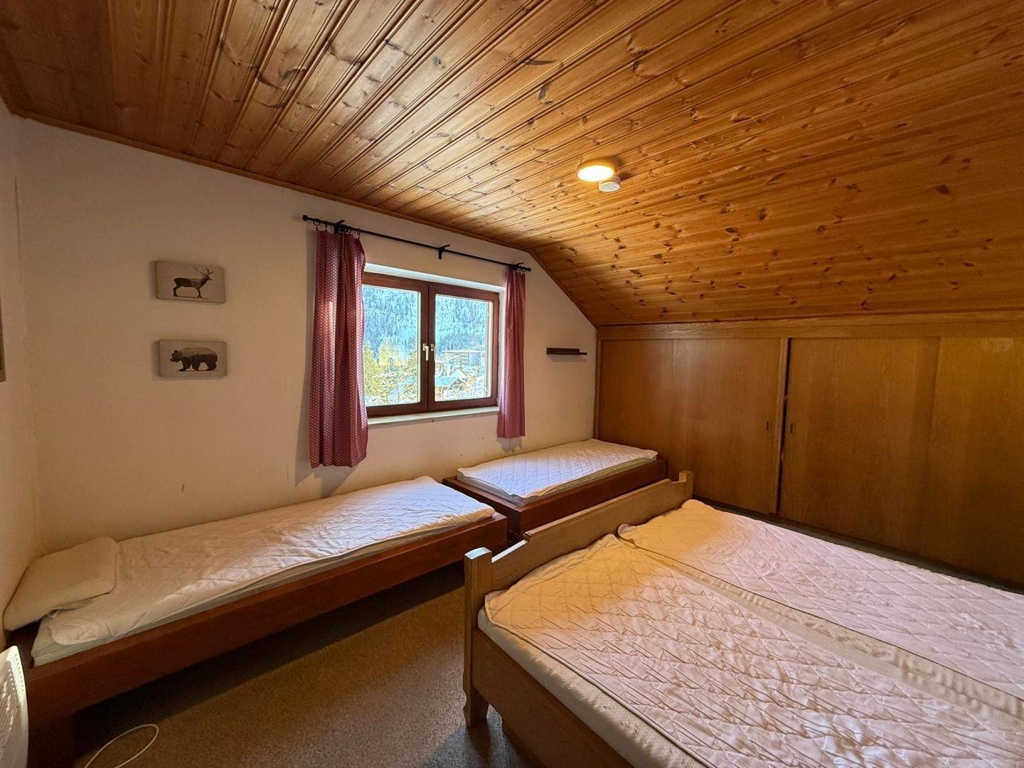 Schlafzimmer mit Holzdecke, drei Einzelbetten und einem Fenster mit Blick auf die verschneite Landschaft.