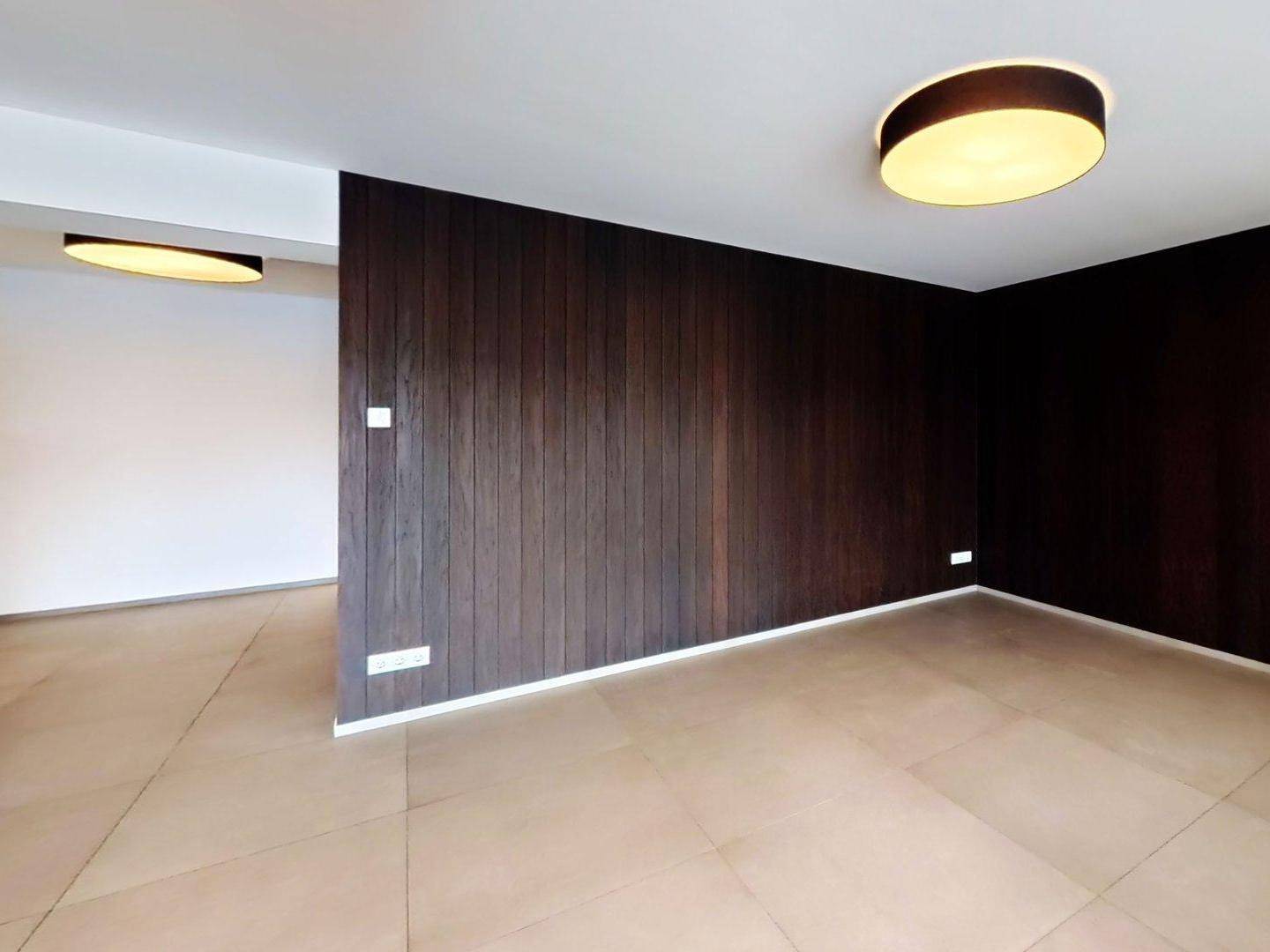 Innenraum mit dunkler Holzwandverkleidung und modernen Deckenleuchten.