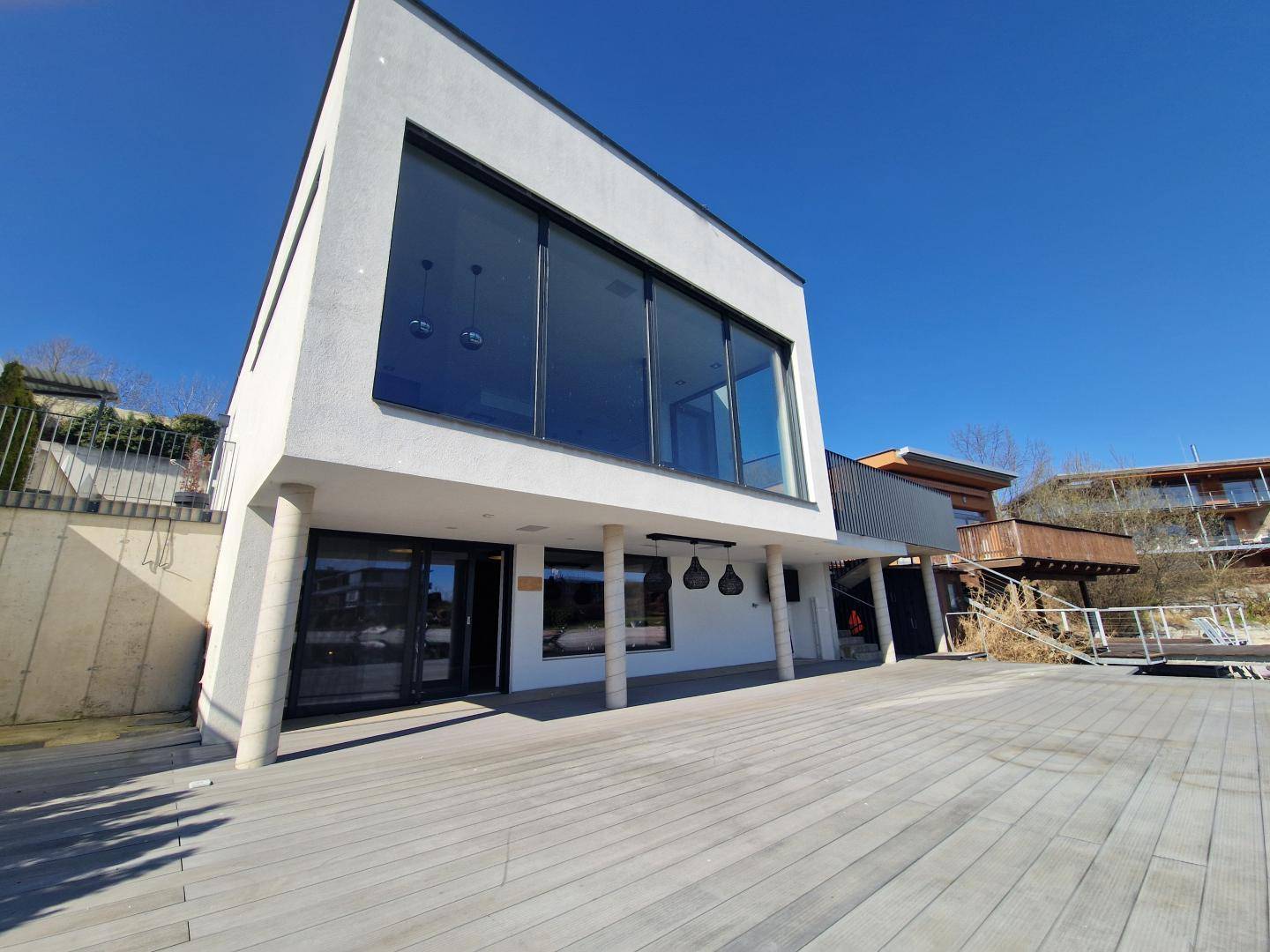 Moderne Architektur mit großen Glasfronten und einer weitläufigen Holzterrasse am Wasser.