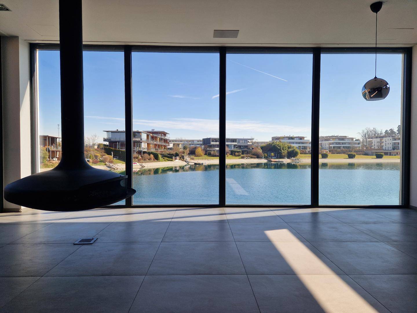 Heller Wohnbereich mit schwebendem Kamin und beeindruckendem Panoramablick auf den See.