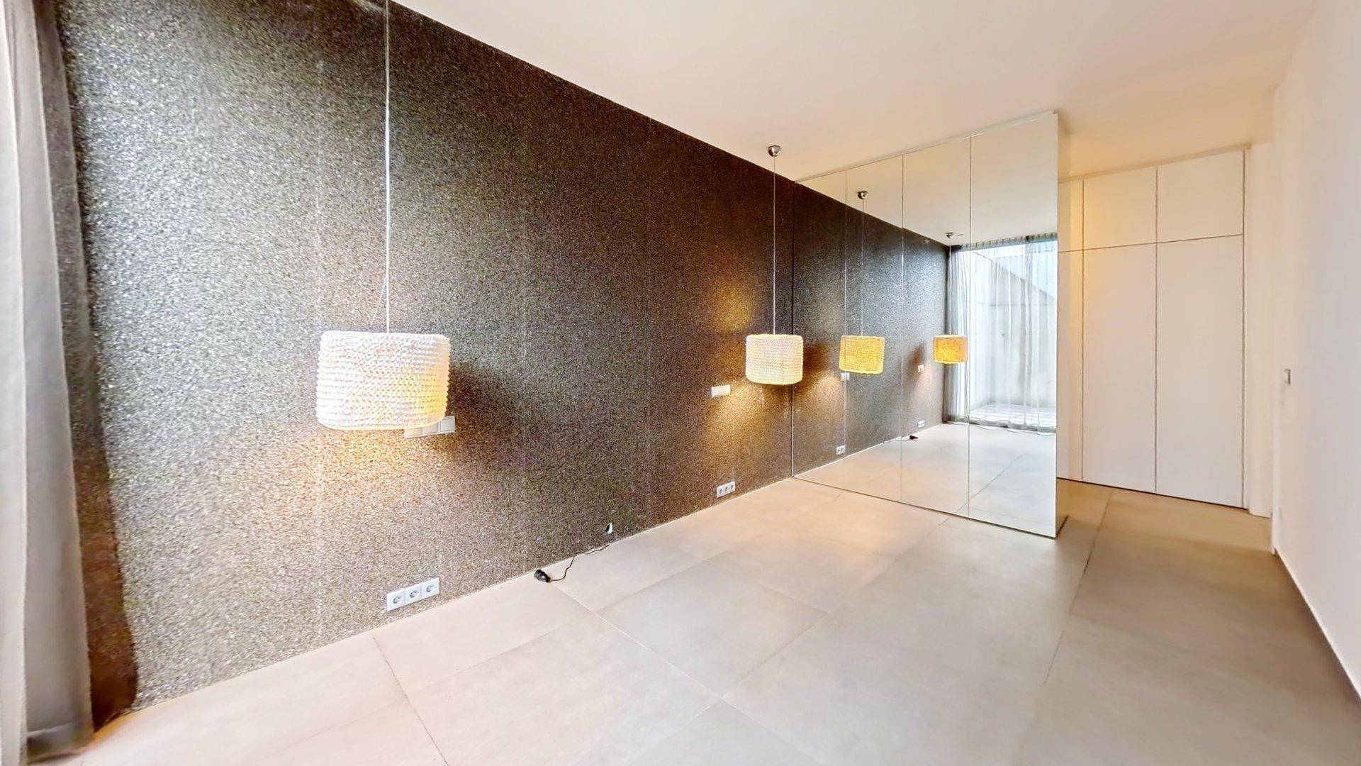 Heller Raum mit glitzernder Akzentwand, Spiegelfronten und modernen Hängelampen.